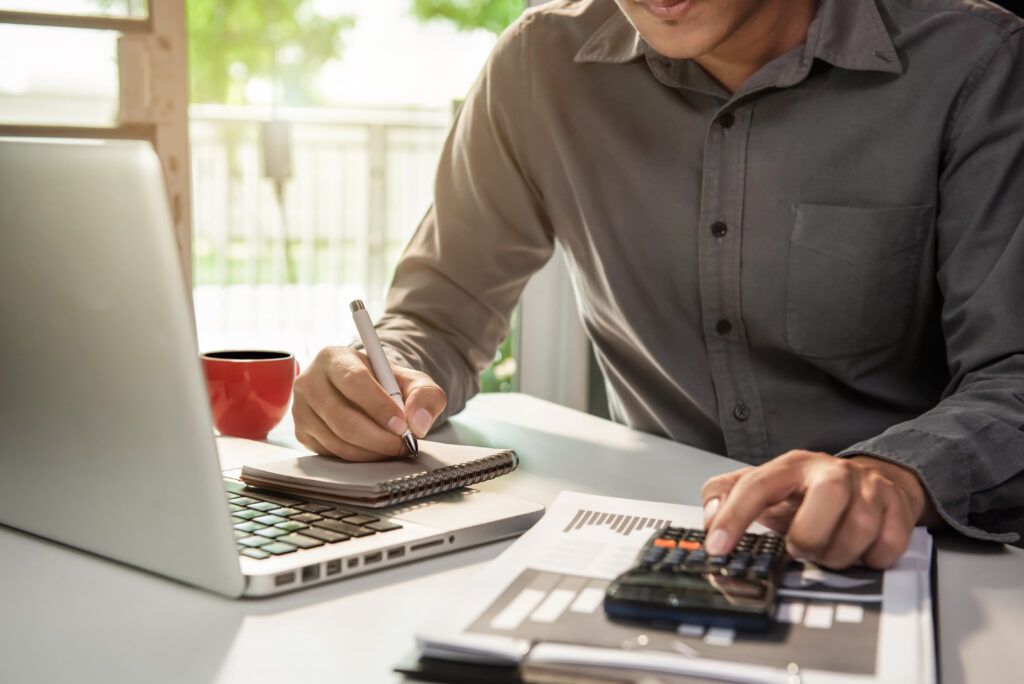 Hombre calculando el presupuesto de ahorro energético con una calculadora y tomando notas en un despacho luminoso.