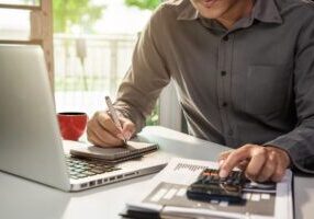 Hombre calculando el presupuesto de ahorro energético con una calculadora y tomando notas en un despacho luminoso.